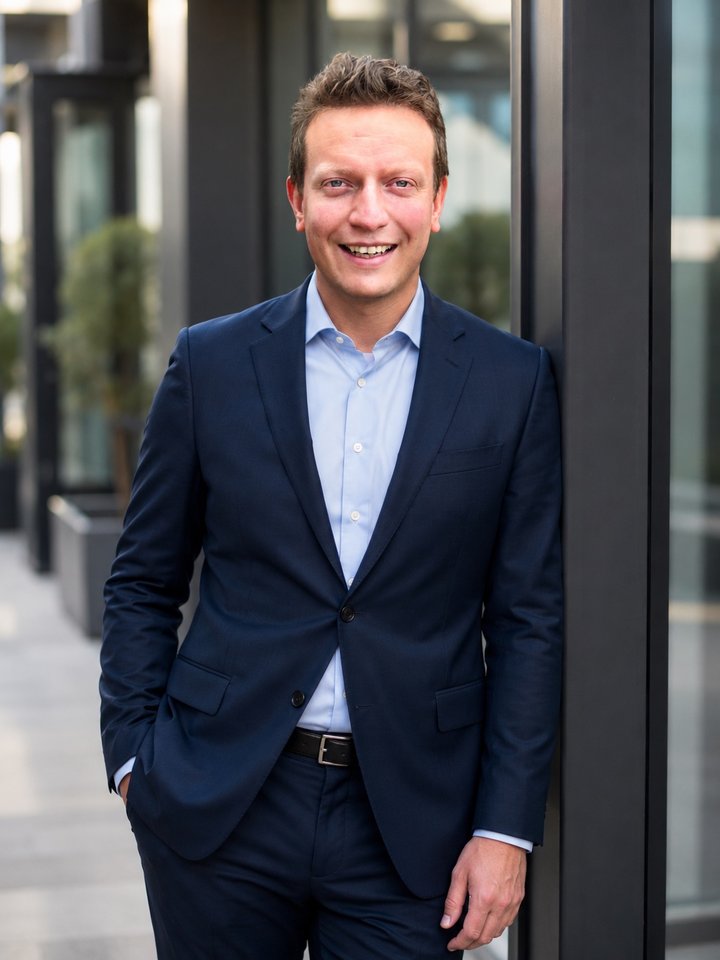 Jonathan Hendry in a navy suit, standing beside a modern building